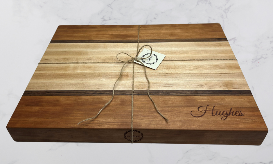 Wooden cutting board with 'Hughes' custom engraved and twine and Willow boards tag on marble surface.