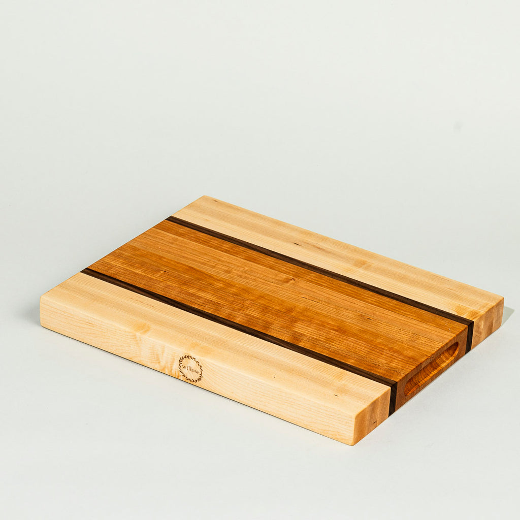 A wood cutting board with a striped design, featuring natural Vermont hardwoods and Willow logo engraved on the side.