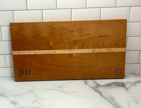 Handmade wood cheese board with 'JFH' monogrammed on a marble surface with tiled wall background