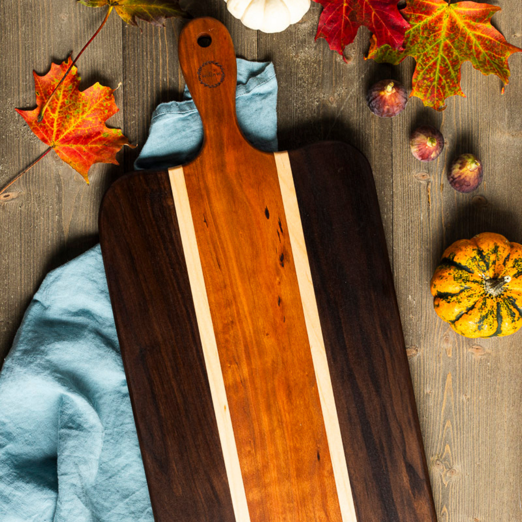 Willow Wood Charcuterie Board made of walnut and cherry with fall leaves, pumpkins and figs around it.