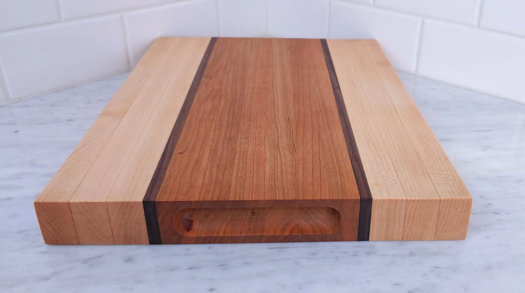 End of handmade wood cutting board showing the finger grips on marble countertop