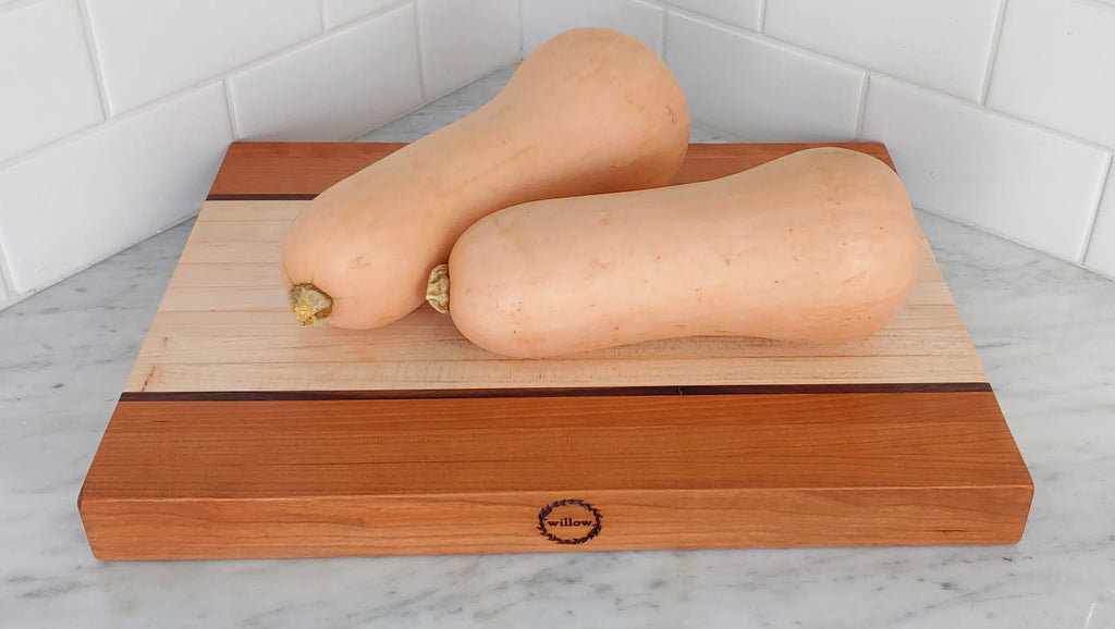 Thick wood cutting board made of Vermont cherry and maple with two butternut squash on marble countertop.